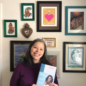 Smiling woman standing in front of a gallery wall holding a Becoming journal with Michelle Obama on the cover.
